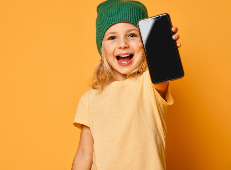 Smiling little girl kid in pink modern hat showing blank screen of mobile phone
